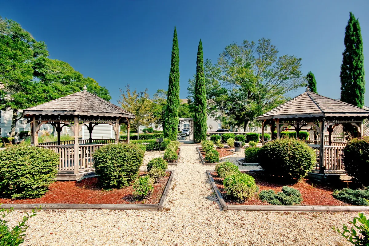 A tranquil garden space featuring charming gazebos, tall cypress trees, and colorful flower beds. The scene is imbued with intimacy and natural beauty, ideal for quiet conversations or intimate outdoor dinners, especially during magical sunsets.