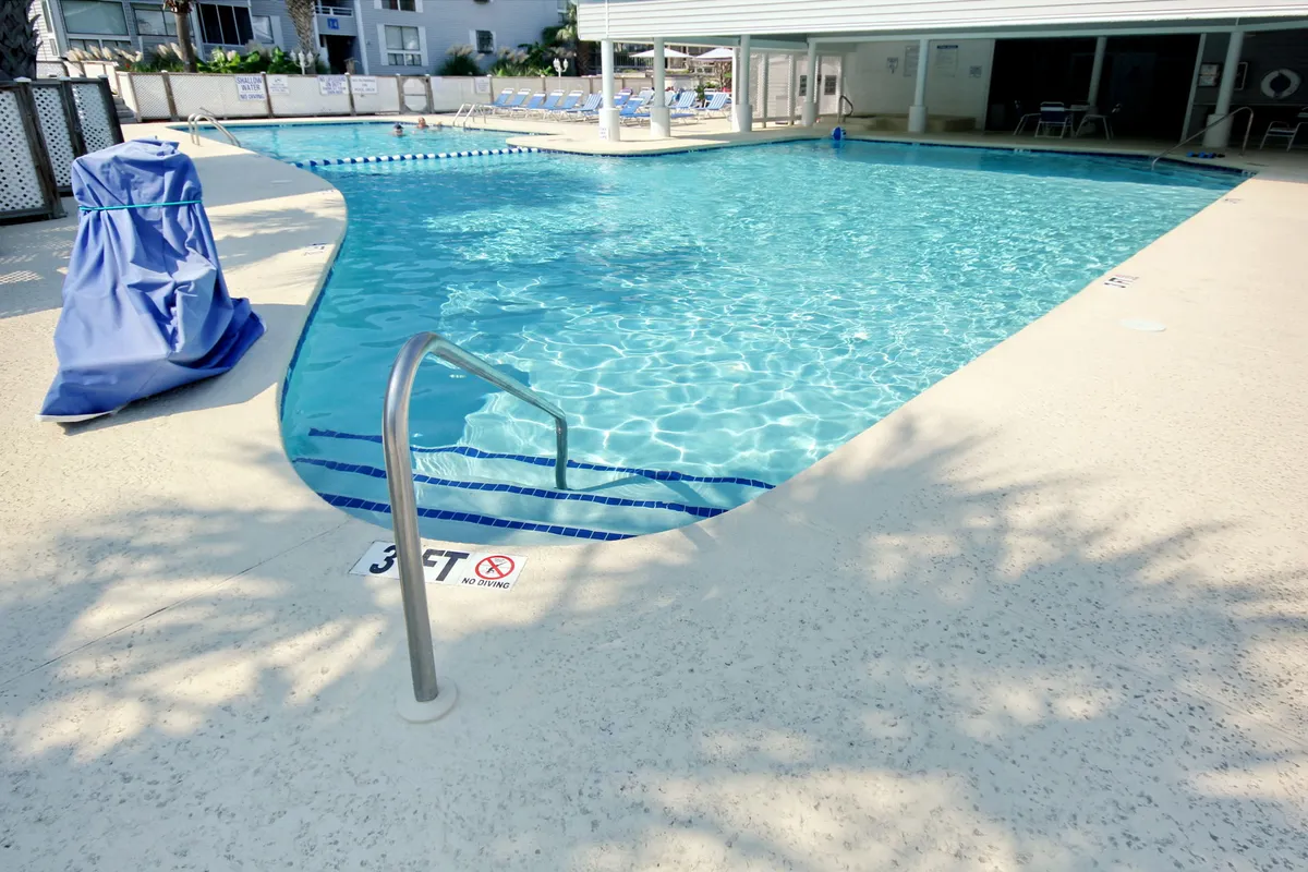A sparkling swimming pool is the focal point, surrounded by lounge chairs and a bright, relaxing atmosphere. The scene emphasizes leisurely swimming, sunbathing, and socializing by the water—activities central to vacation community living.