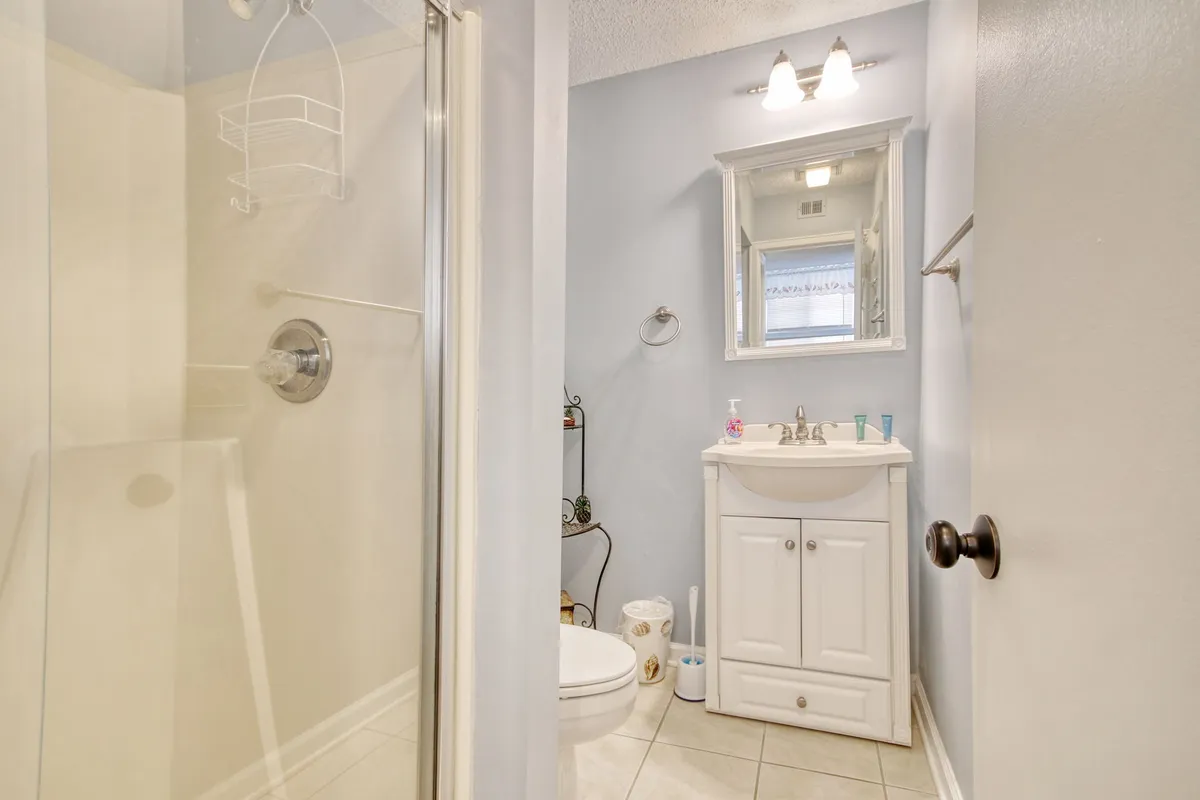 A modern bathroom is showcased here, featuring a spacious shower area, a vanity with mirror, toilet, and a decorative shelf. The atmosphere is fresh and inviting, designed for daily comfort and relaxation.