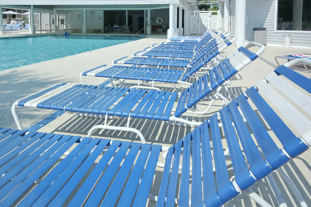 A spacious outdoor swimming pool area with lounge chairs and the surrounding residential building. The scene is tranquil, showcasing an ideal space for relaxation, sunbathing, and socializing with neighbors.