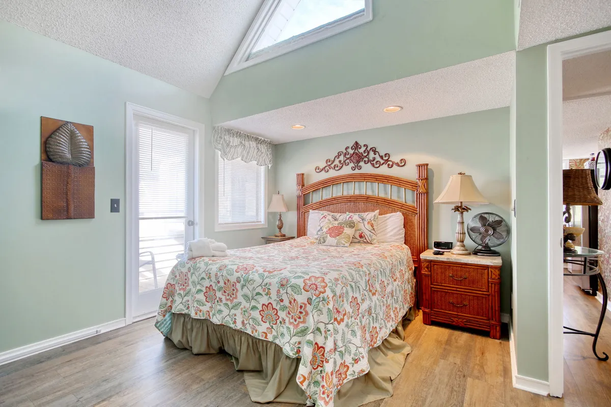 The image features a serene bedroom with a bed adorned in floral bedding, complemented by a wooden headboard, side tables with lamps, and decorative wall art. Natural light fills the space, creating a peaceful ambiance ideal for restful mornings.